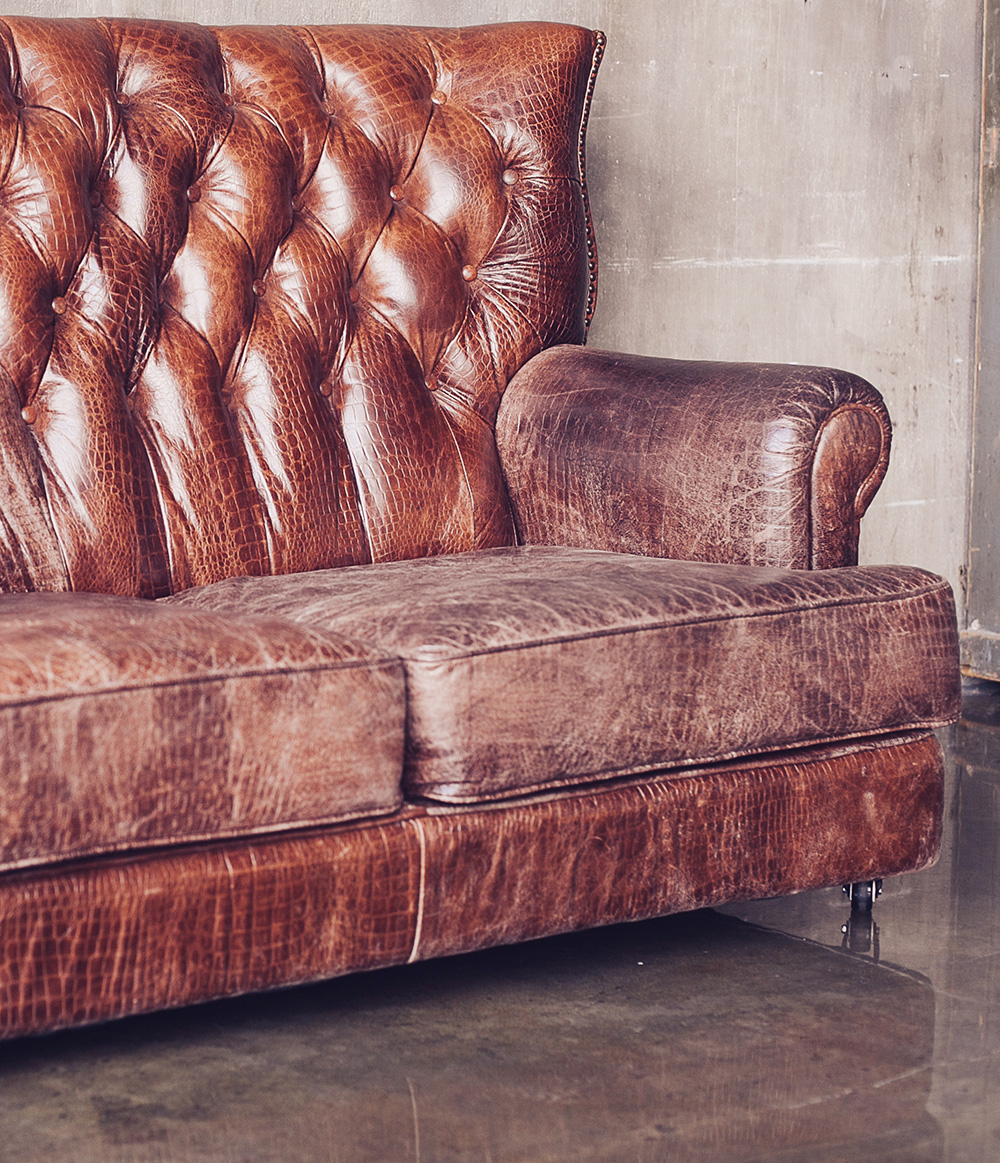 del av sliten rödbrun soffa i läder av chesterfieldmodell
