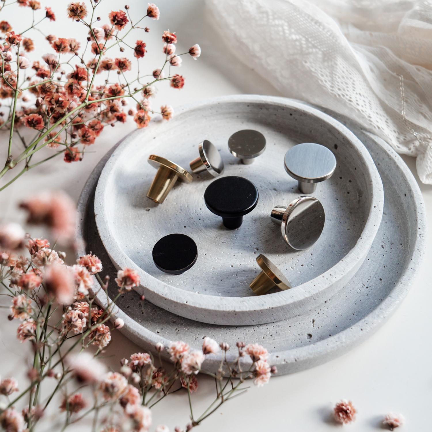 Köksknopp Folke i svart, mässing och nickel  på cementbricka med smycken och rosa blommor i alla hjärtans dag inspiration