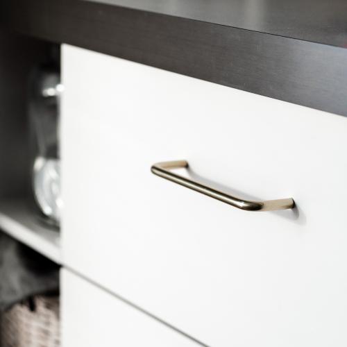 Minimalistiskt kökshandtag i nickel mot en vit kökslucka och grå bänkskiva