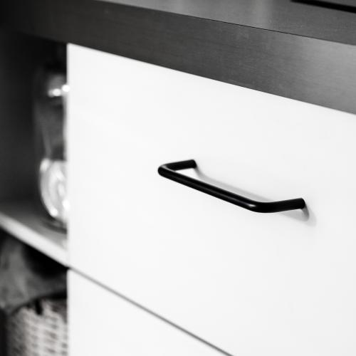 Minimalistiskt kökshandtag i svart mot en vit kökslucka och grå bänkskiva