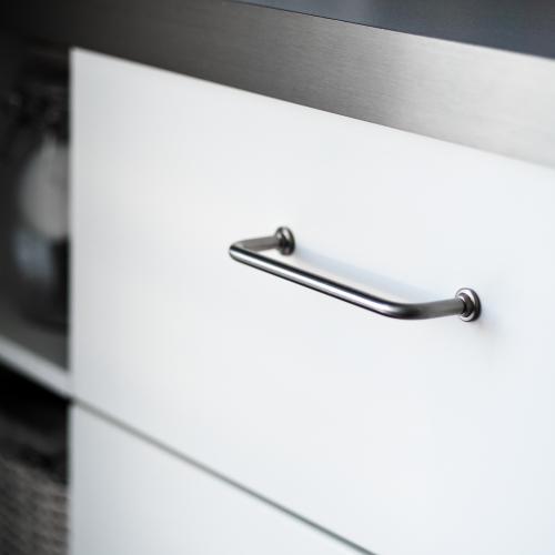 Handtag 1353 i rostfri look mot vit lucka och grå bänkskiva.