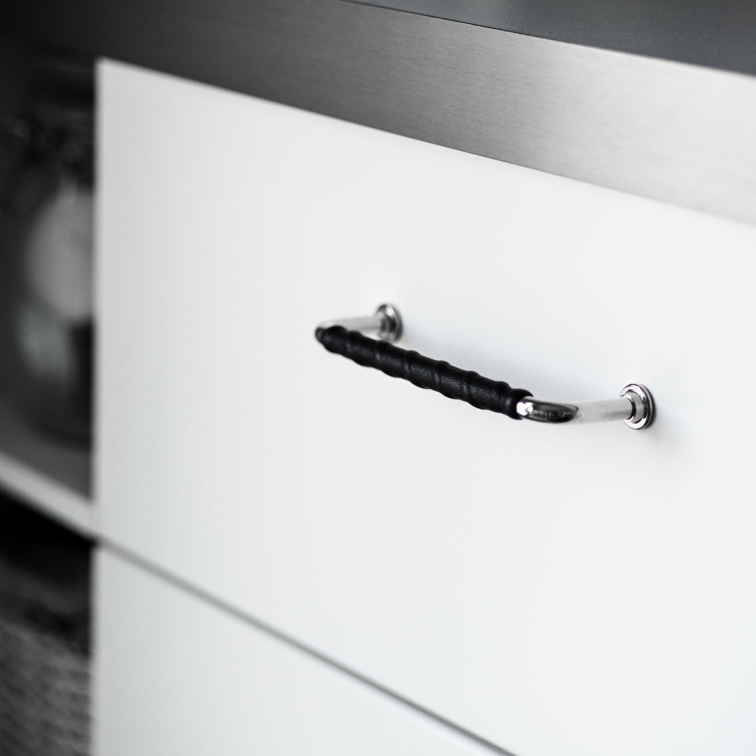 Läderklätt handtag 1353 i nickel och svart mot vit lucka och grå bänkskiva.