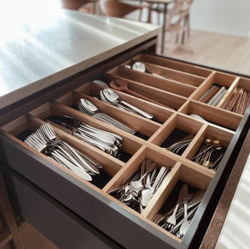 Besticklåda i ek i en mörkgrå kökslåda mot ljust trägolv och beige bänkskiva med vårljus