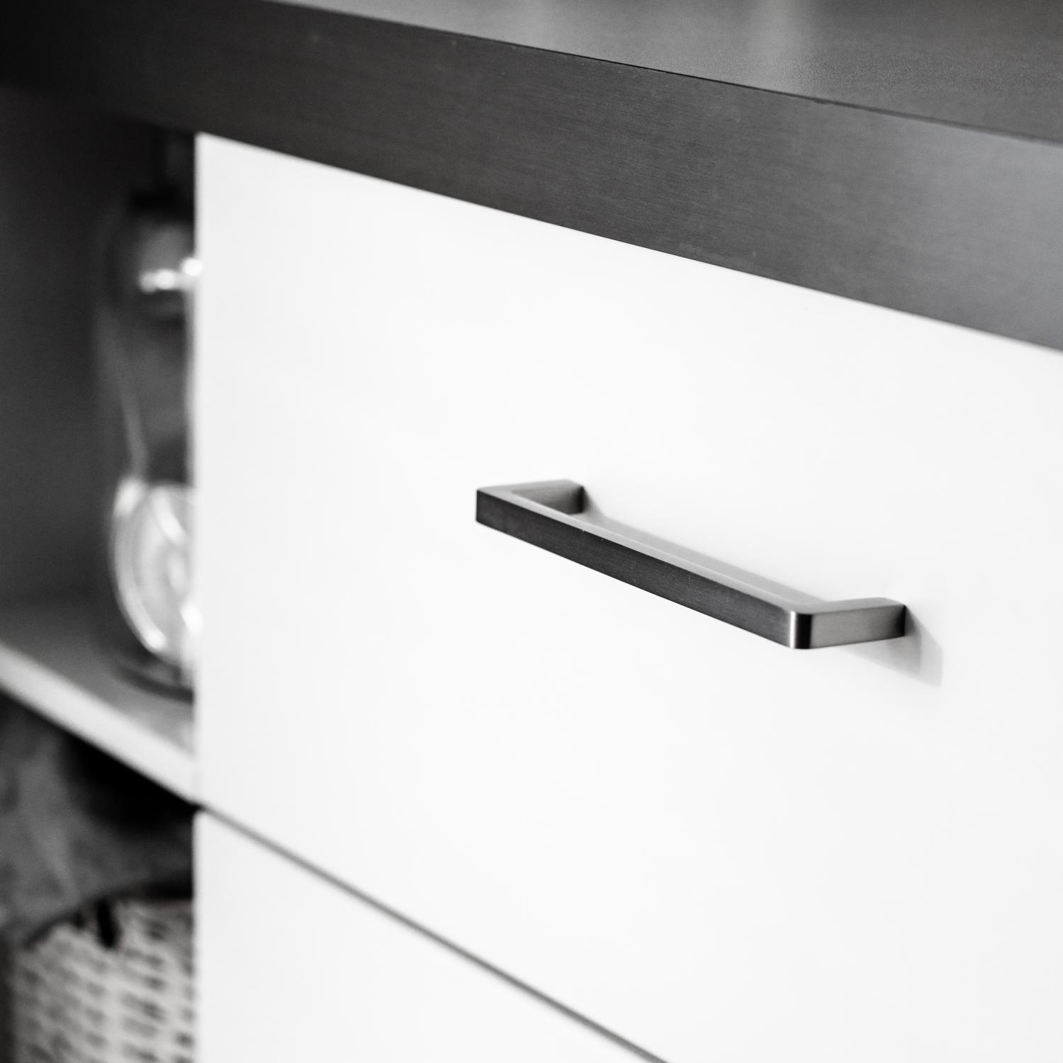 Kökshandtag i rostfri look mot en vit kökslucka och grå bänkskiva