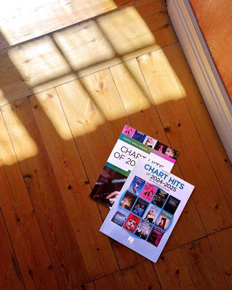Easy Piano Chart Hits of 2024-2025, bokomslag med 12 populära singlar I miniatyromslag, liggandes på trägolv.