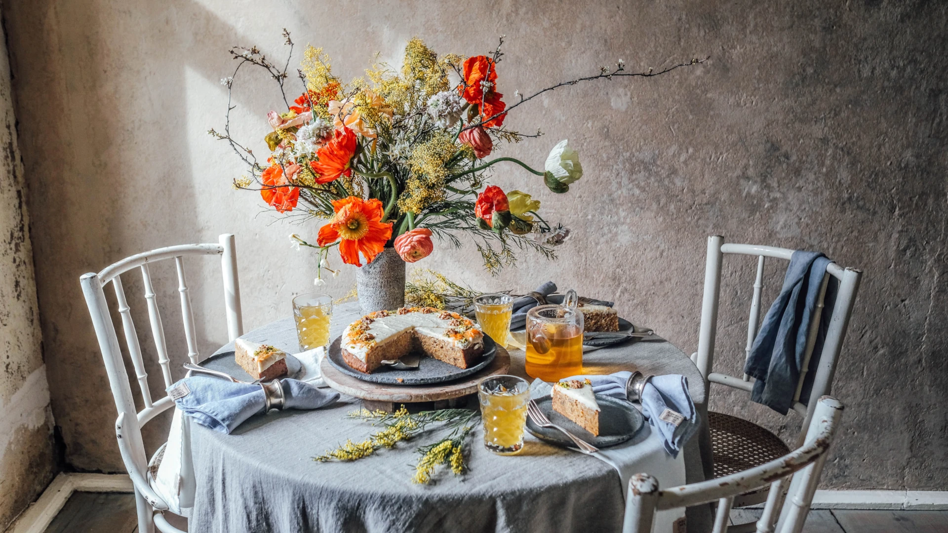 Rustik sommardukning med grå linneduk, blommor och frukost i ett ljust rum