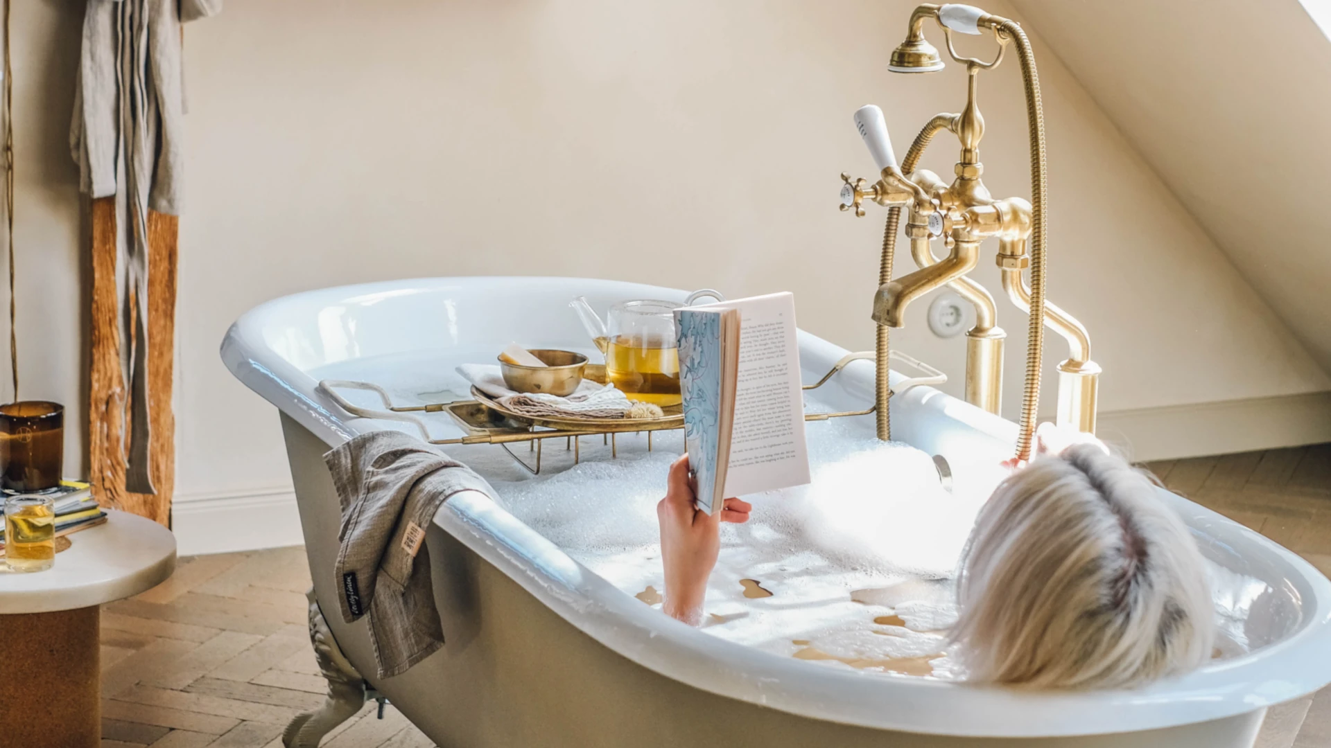 Person läser en bok i ett badkar med linnehandduk över kanten.
