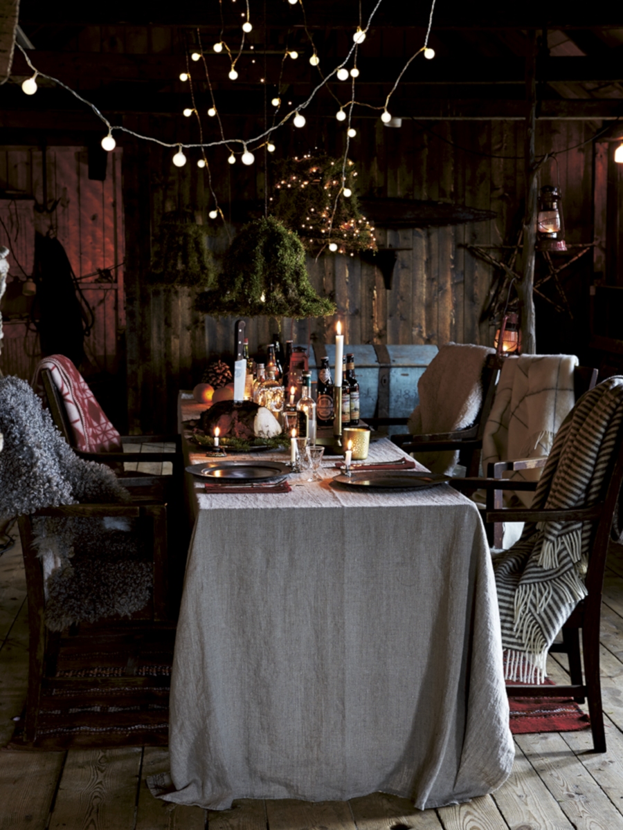 En mörk, elegant dukning med staplade blå och vita tallrikar, glas och en svart bricka med vikta servetter. Bruna, gröna glasflaskor, ljushållare med vita ljus och grönt bladverk fulländar arrangemanget.