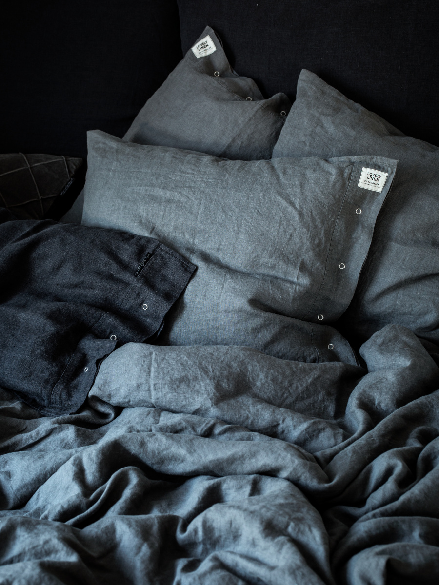 En fint obäddad säng med mörkgrå linnelakan och kuddar.