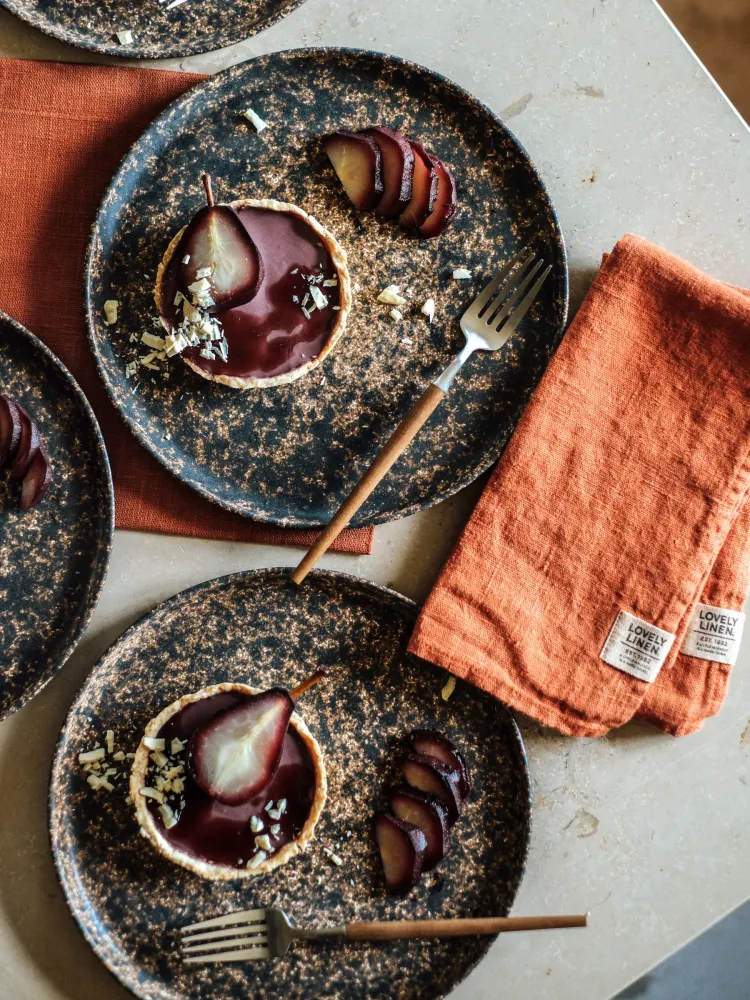 Linen napkins in Lovely Cayenne beside rustic plates with dessert and plums.