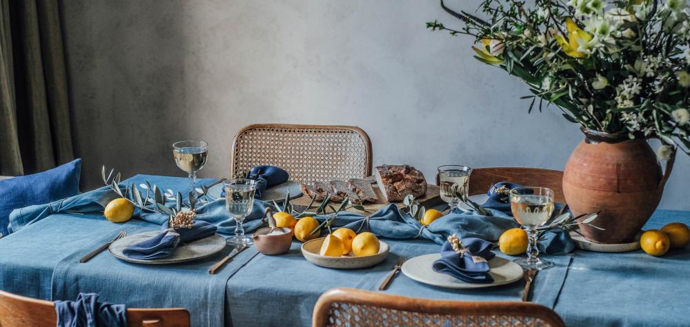 Ett vackert dukat bord med blå linnetextilier, dekorerat med citroner och blommor i en rustik vas