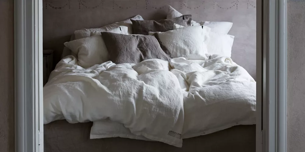 Varför sova i Lovely Linens linnelakan? Vit bäddad säng med sängkläder i linne i ett rustikt rum med naturliga inslag och enkel inredning.
