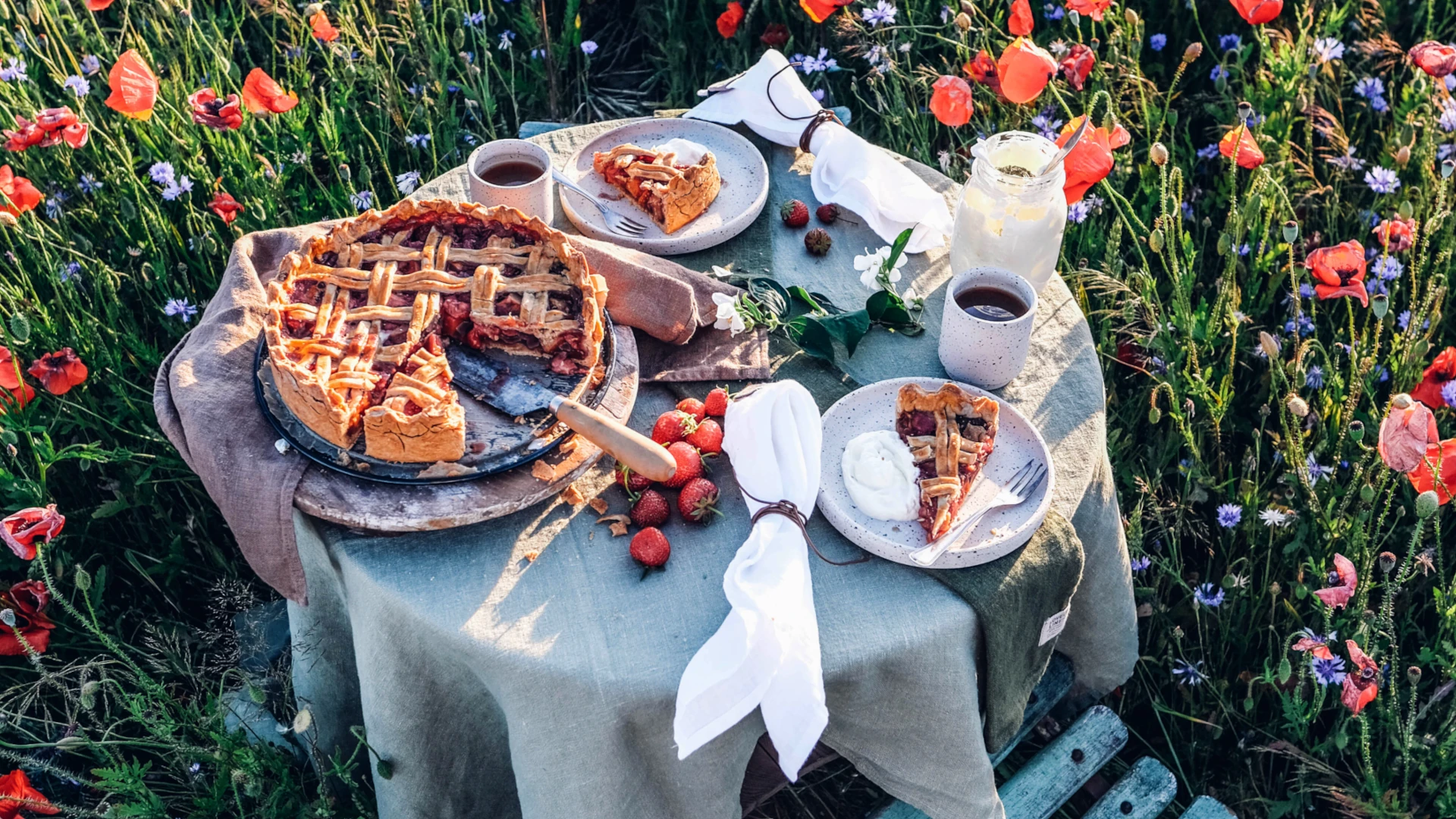Summer table setting in a blooming meadow with a plate, cake and strawberries.