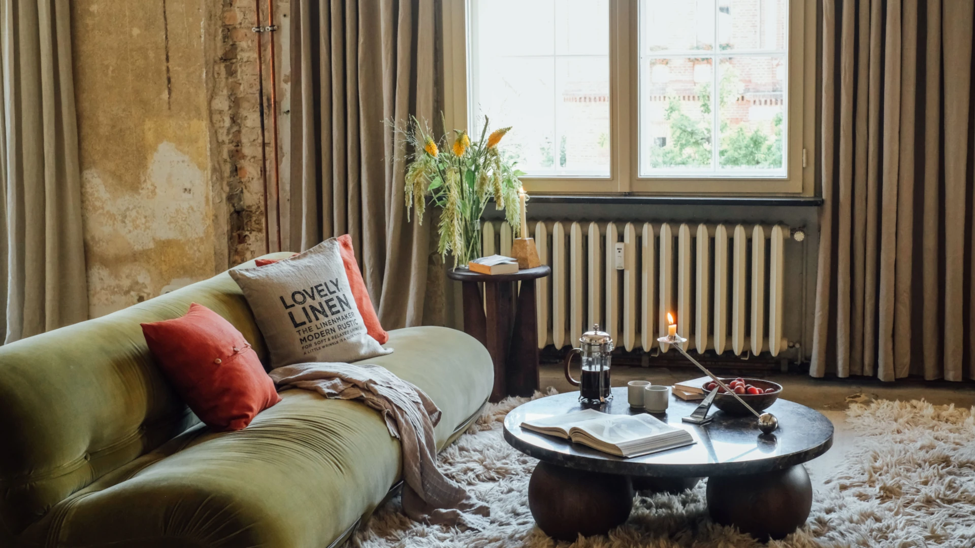 Grön soffa med roströda och gråbeige kuddar, en beige pläd och långa beige gardiner.
