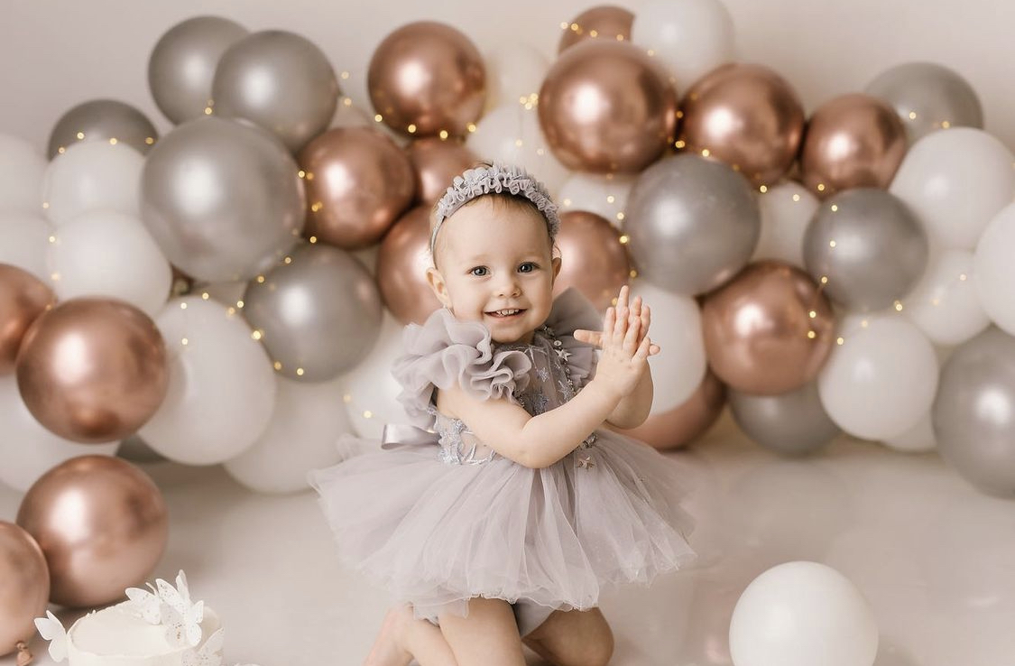 Ballongbåge i roseguld, silver och vitt med en bebis framför