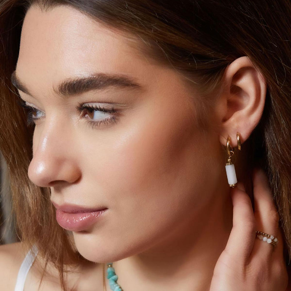 Kvinna använder guldringar med vita avlånga stenar i öronen.