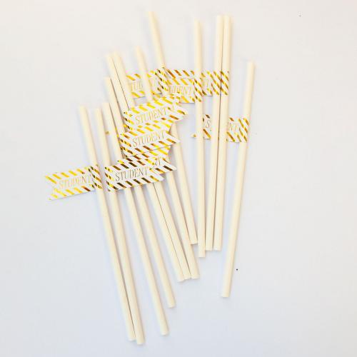 Vita papperssugrör med en flagga på och texten student. Gulddetaljer