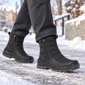 En man i mörka byxor går utomhus i ett snöigt vinterlandskap. Han bär svarta, quiltade Josef Seibel Alaska 51 vinterkängor med synlig dragkedja och en robust, greppsäker sula på snötäckt mark.