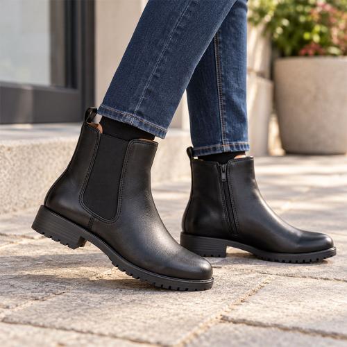En kvinna i blå jeans bär svarta Chelsea-boots i skinn från Park West utomhus. Kängorna har en elastisk panel på yttersidan, en diskret dragkedja på innersidan och en greppsäker gummisula.