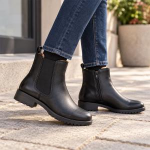 En kvinna i blå jeans bär svarta Chelsea-boots i skinn från Park West utomhus. Kängorna har en elastisk panel på yttersidan, en diskret dragkedja på innersidan och en greppsäker gummisula.