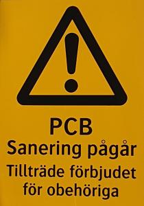 En gul  varningsskylt i plåt med texten PCB  Sanering pågår tillträde förbjudet för obehöriga