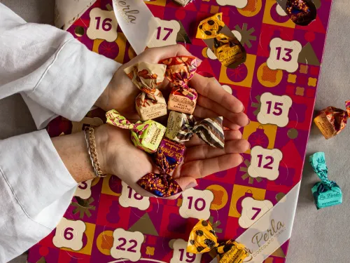 Adventskalender i rött med chokladpraliner från italien. En hand som plockar upp en pralin