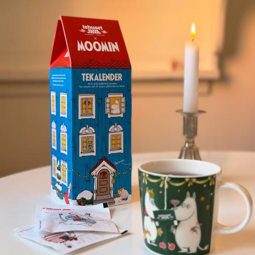 Tekalender med tepåsar på ett bord. Motiv av muminfamiljens hus, ett blått hus med rött tak.