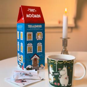 Tekalender med tepåsar på ett bord. Motiv av muminfamiljens hus, ett blått hus med rött tak.